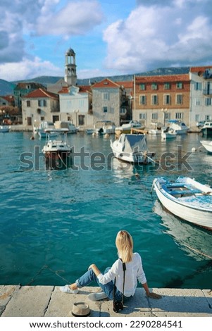 Tourism concept. Young traveling woman enjoying the view of Kastel Castle sitting near the sea on Croatian coast.