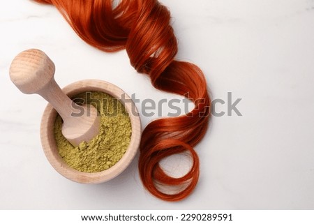 Mortar of henna powder and red strand on white marble table, flat lay with space for text. Natural hair coloring