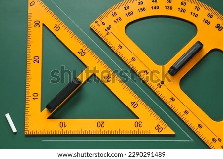 Protractor, triangle and chalk on green chalkboard, flat lay