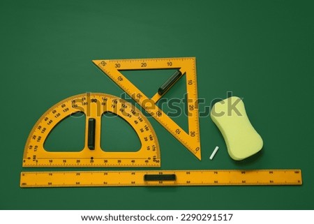 Protractor, triangle, ruler and sponge on green chalkboard, flat lay