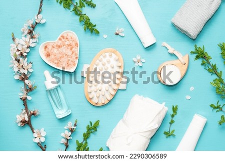 Spa and wellness concept. Rolled towels, massage brushes, Himalaya salt, cosmetic creams, balms, masks and serums and blooming apricot branches on bright blue background top view.