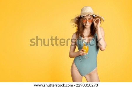 Fit lady in swimsuit and straw hat posing with tropical fruit cocktail over yellow studio background, panorama with free space. Young woman having fresh drink, enjoying beach party