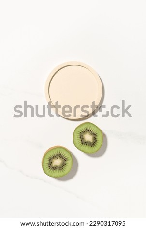 Beauty cosmetics product presentation flat lay mockup scene with beige circle shape and kiwi fruits on white marble table with copy space. Trendy sunlight, vertical format. Studio photography.