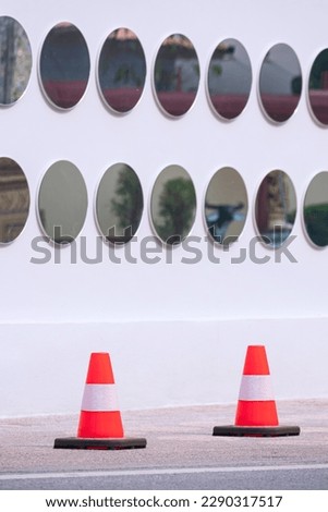 Two red and white traffic cones for no parking on the floor with blurred background of circle mirrors rows on exterior white coffee shop wall decoration background in vertical frame 