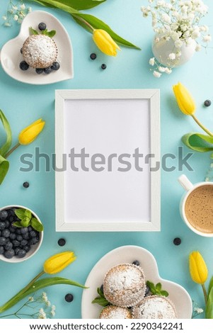 Trendy mother's day celebration table setting concept. Top vertical view of cupcakes, tulips, and coffee on a pastel blue background with an empty frame for text or greeting message
