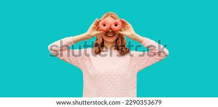 Portrait of happy funny laughing woman covering her eyes looking for something looking through donuts as binoculars having fun on blue background Royalty-Free Stock Photo #2290353679