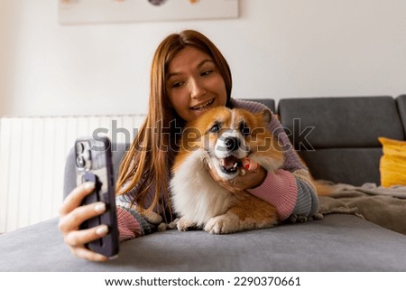 a young girl with a corgi dog and taking selfie with pet on smartphone camera. Concept stay at home, friendship with dog, taking picture. 