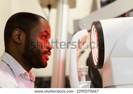 A dark-skinned man is going to undergo a vision test using a corneal topograph to examine the cornea. Concept of corneal topographial in men. Royalty-Free Stock Photo #2290370667
