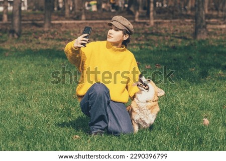 Friendship Concept. Excited beautiful caucasian woman taking selfie with her welsh corgi pemroke dog in the park,corgi licking her face. High quality photo