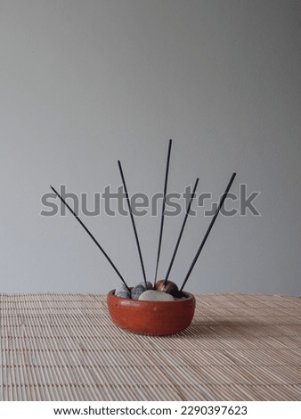 Ceramic incense holder filled with decorative stones and 5 long stick incense on bamboo cane table with white background
