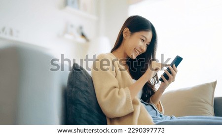 Happy young asian woman relax on comfortable couch at home texting messaging on smartphone, smiling girl use cellphone, chatting online message, shopping online from home Royalty-Free Stock Photo #2290397773