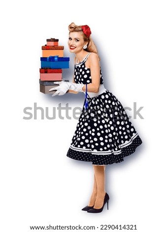 Big sales discounts, rebates offers ad concept - full body image of happy smiling, cheerful  beautiful woman in pin up black dress, hold gift boxes stack, isolated against white background