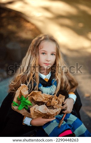 A little girl with blond hair sits on a suitcase and conjures with a magic wand. The sorceress creates magic on the street. Fairy-tale image of a child of a witch. halloween