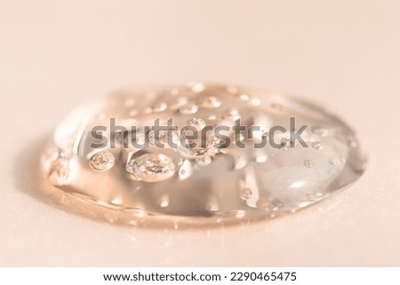 Drop of transparent face serum on a beige background, flat lay. Liquid transparent texture macro.