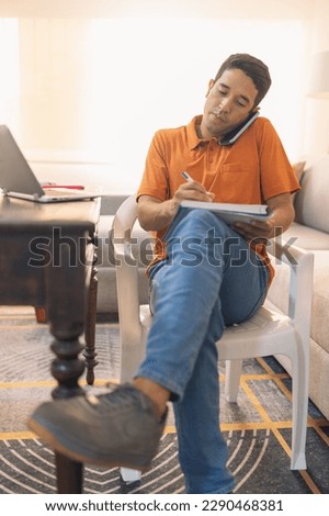 Vertical photo of a man taking notes and talking with a mobile phone in a home office