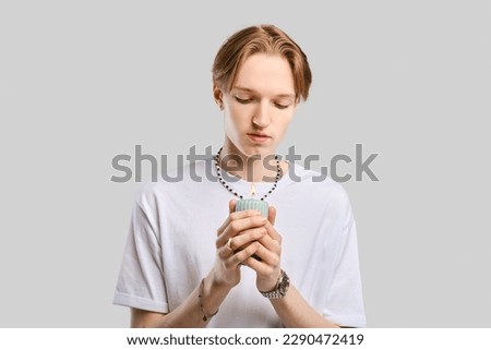 Young man holds candle in hand over grey studio background