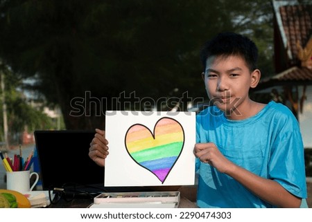 Asian boy in blue t-shirt sitting and spending his free time with drawing heart picture by using watercolor, concept for summer vacation of LGBT teenagers around the world.
