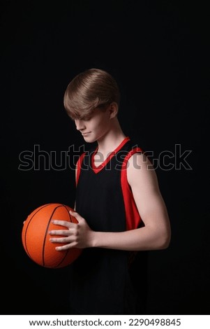 Teenage boy with basketball ball on black background