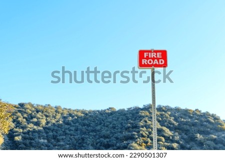 Fire Road Sign standing out against the beautiful blue sky and dense forest in California.