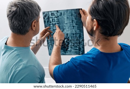 Manual therapist viewing X-ray of backbone with his male patient with spinal problem during medical consultation at hospital Royalty-Free Stock Photo #2290511465