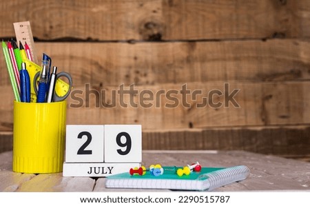 July calendar background with number  29. Stationery pens and pencils in a case on a wooden vintage background. Copy space notepad with pencils and calendar. Planner place for text.