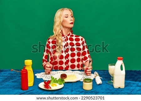 Wonderful, senior woman having dinner, eating cutlet and mashed potato against green studio background. Food pop art photography. Complementary colors. Concept of food, taste, creativity, retro style.
