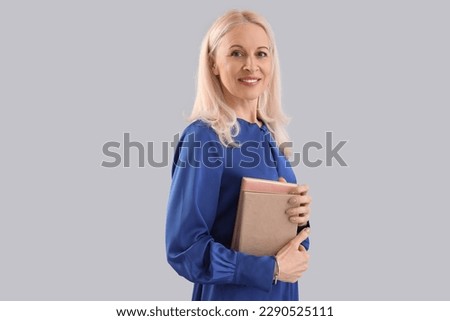 Mature woman with books on grey background