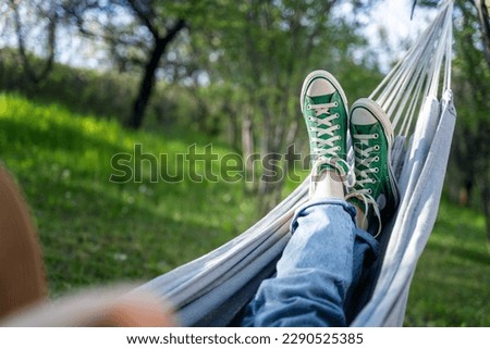Women's legs shod in green sneakers on a hammock in a summer garden. Summer holidays vacation concept Royalty-Free Stock Photo #2290525385