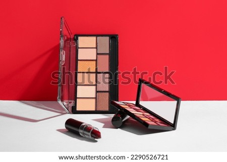 Lipstick with eyeshadows on table near red wall Royalty-Free Stock Photo #2290526721