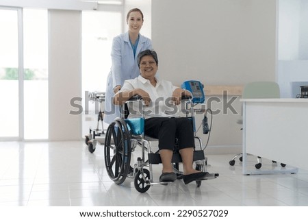 Doctor helping senior patient push wheelchair in hospital interior.