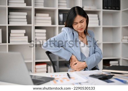 Tired and unwell millennial Asian businesswoman suffering from her office syndrome, feeling back pain during work at her desk. Health problems concept Royalty-Free Stock Photo #2290530133