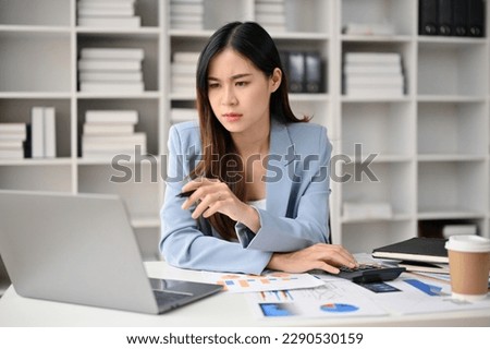 Professional and focused millennial Asian businesswoman looking at her laptop screen, planning her project and working in her office.