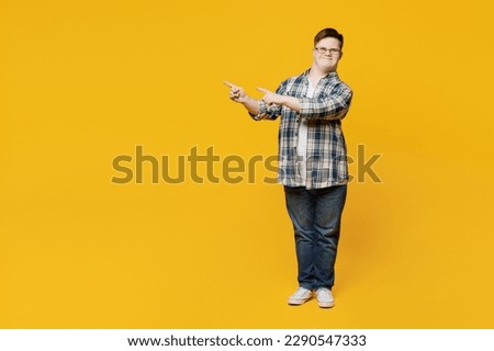 Full body young happy man with down syndrome wear glasses casual clothes point index fingers aside on workspace area isolated on pastel plain yellow color background. Genetic disease world day concept Royalty-Free Stock Photo #2290547333