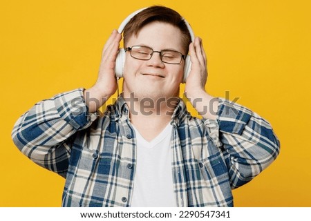 Young smiling satisfied man with down syndrome wears glasses casual clothes headphones listen to music close eyes isolated on pastel plain yellow color background. Genetic disease world day concept Royalty-Free Stock Photo #2290547341