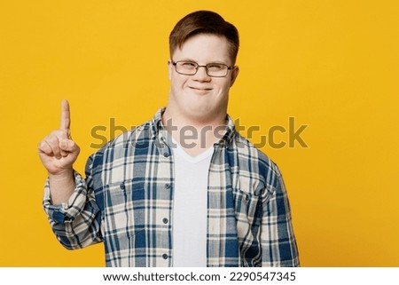 Young fun smiling man with down syndrome wearing glasses casual clothes holding index finger up with great new idea isolated on pastel plain yellow color background. Genetic disease world day concept