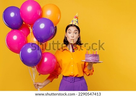 Happy fun amazed young woman wear casual clothes hat celebrating hold bunch of colorful air balloons cake with candles blow pipe isolated on plain yellow background Birthday 8 14 holiday party concept