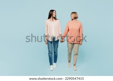 Full body happy smiling elder parent mom with young adult daughter two women together wear casual clothes hold hands walk go look to each other isolated on plain blue background. Family day concept Royalty-Free Stock Photo #2290547415
