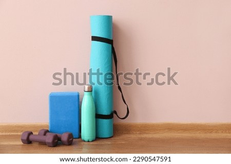 Dumbbells with fitness mat, block and bottle near pink wall