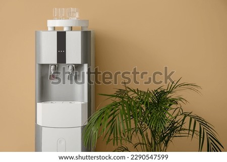 Modern water cooler and houseplant on beige background Royalty-Free Stock Photo #2290547599