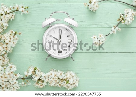 Blooming spring branches and alarm clock on green wooden background Royalty-Free Stock Photo #2290547755