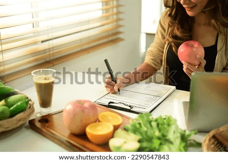 Nutritionist sitting at desk with fruit and vegetable, working on diet plan. Healthy eating, right nutrition and diet concept Royalty-Free Stock Photo #2290547843