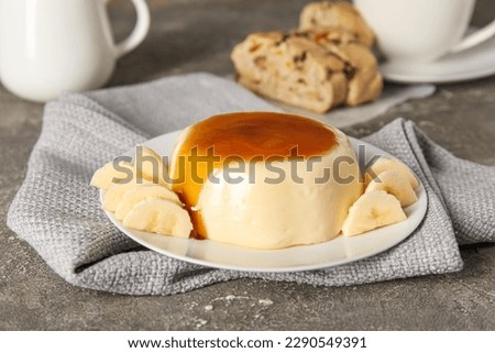 Plate with delicious pudding and bananas covered by caramel syrup on grey grunge background Royalty-Free Stock Photo #2290549391