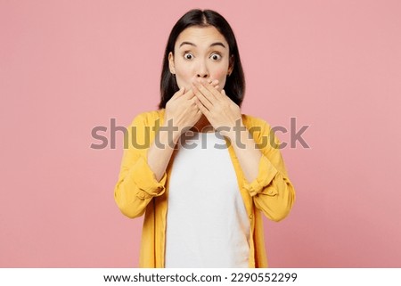 Young shocked fearful sad woman of Asian ethnicity wear yellow shirt white t-shirt look camera cover mouth with hands isolated on plain pastel light pink background studio portrait. Lifestyle concept Royalty-Free Stock Photo #2290552299