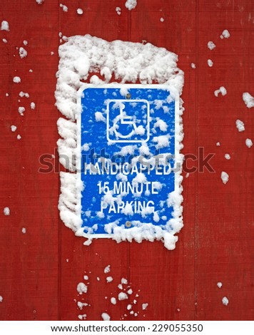 A bright blue handicapped parking sign with snow on sign and siding.