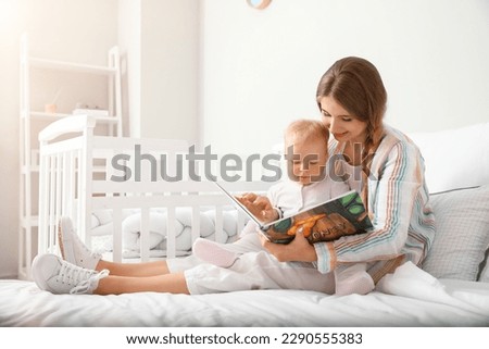 Young mother reading book to her cute little baby on bed Royalty-Free Stock Photo #2290555383