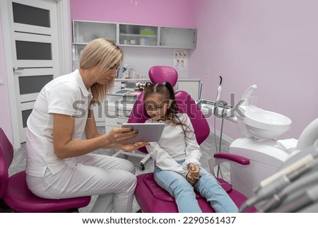 woman dentist shows a cartoon to a girl on a tablet before examining her oral cavity. dentistry for children. review