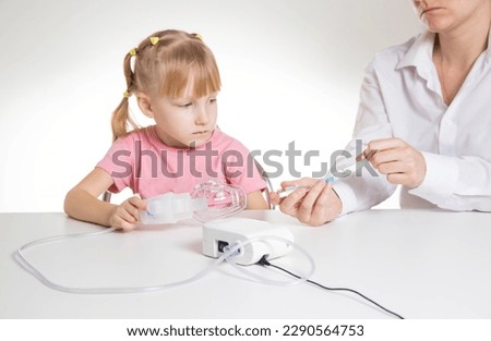 A doctor is putting a drug into a nebulizer for the treatment of respiratory diseases in a little girl 5 years old. Inhalation for the treatment of bronchitis and pneumonia Royalty-Free Stock Photo #2290564753