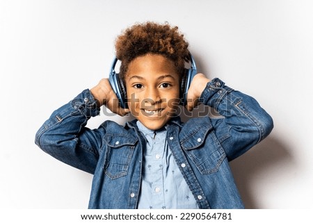 Portrait of a cute 5-6 year old boy with dark skin and afro hair posing on a white background. The child is wearing wireless headphones. Concept of study through recordings, learning by listening