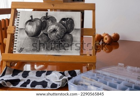 Drawing fruit with charcoal, four apples, on a sketch pad on a portable easel