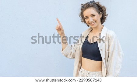 Young woman in sunglasses over gray wall background, pointing finger to the left side. Place for text.